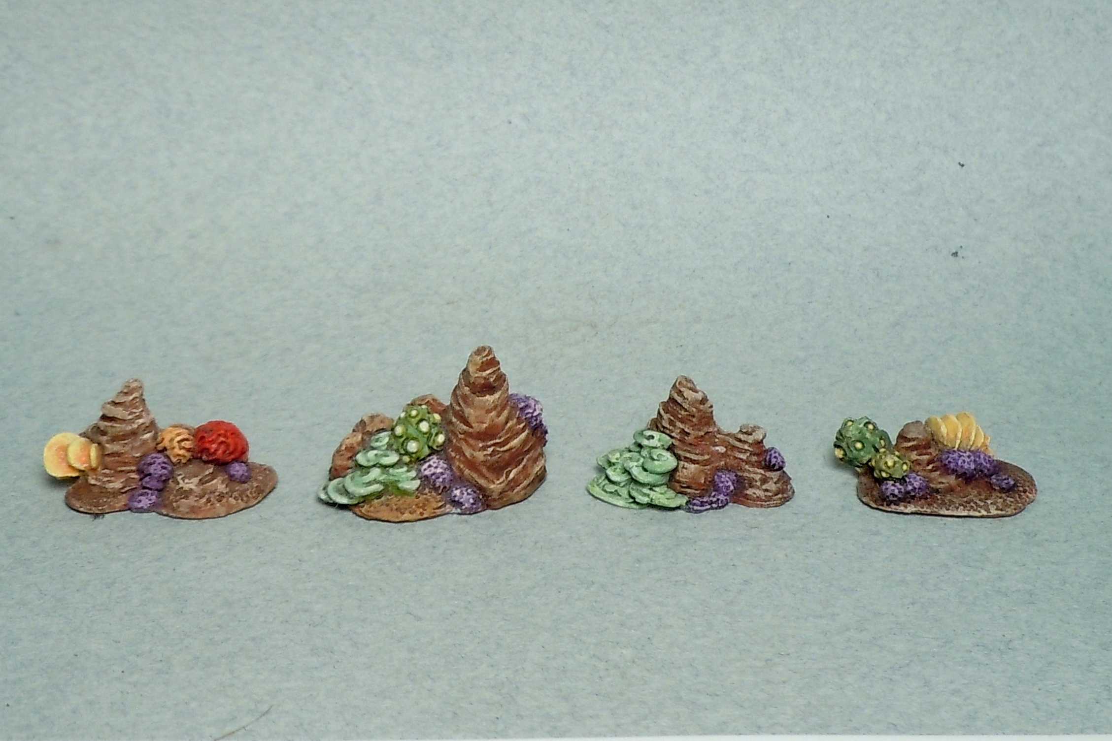Four small painted miniature terrain pieces with colorful red, green, and purple details, resembling coral or rock formations.